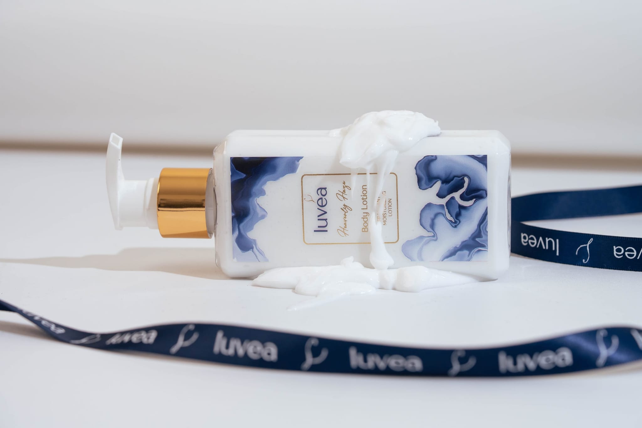 Heavenly Haze lotion bottle resting beside swirls of cream texture and a navy luvéa ribbon